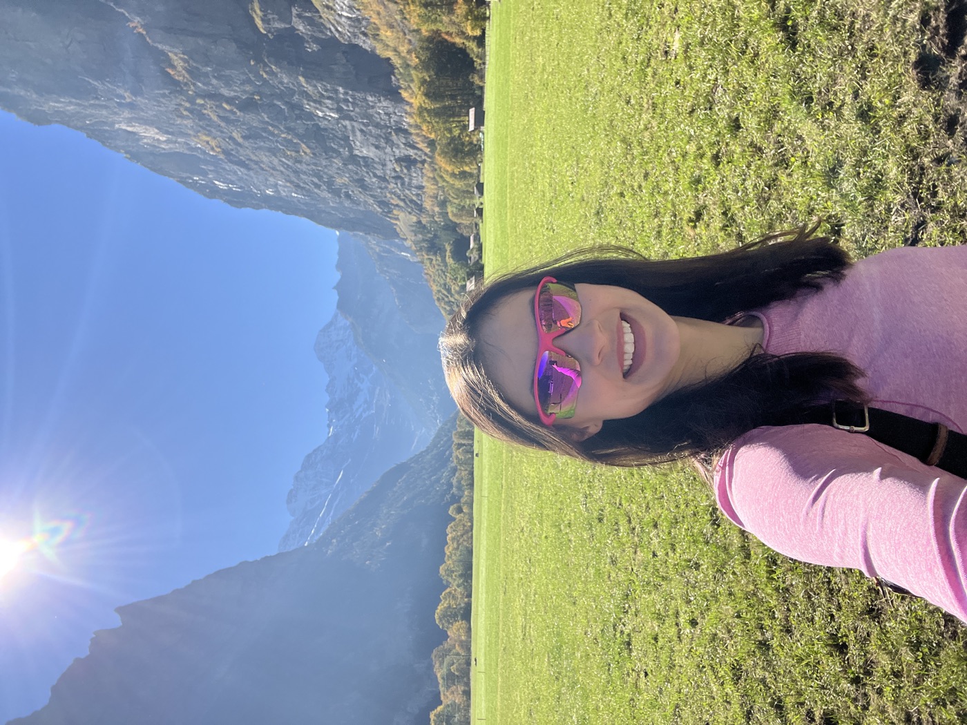 Lilly smiling in a green meadow in Lauterbrunnen, with sheer cliffs on both sides and snowy Alps at the end of the valley.